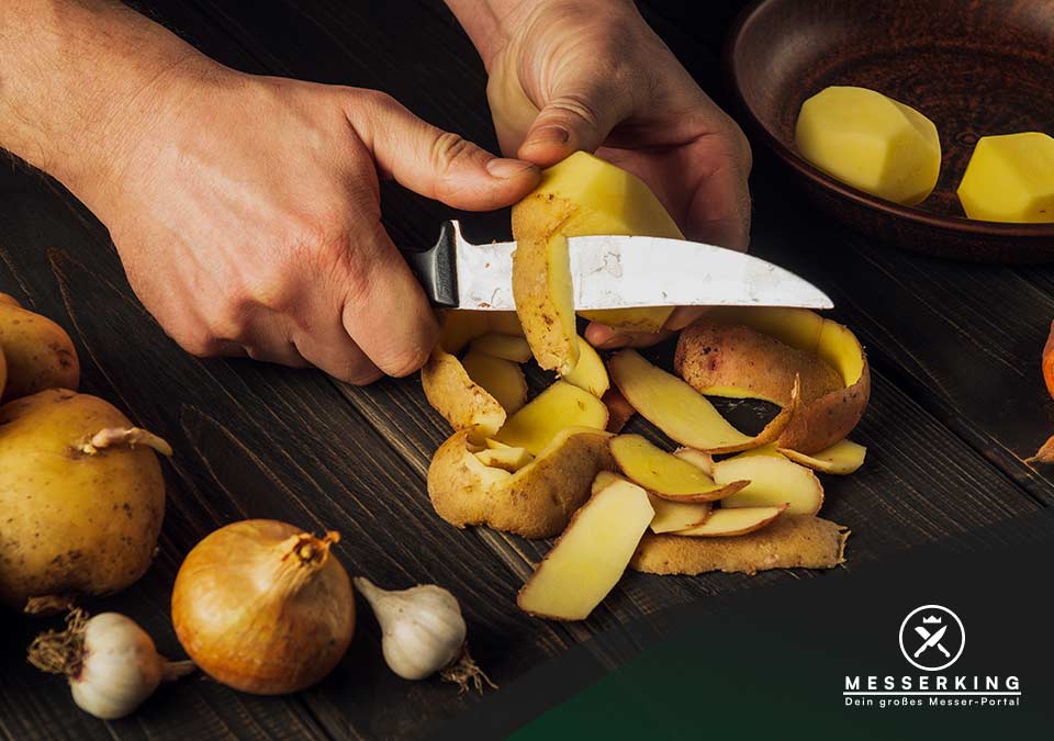 Männerhände schälen Kartoffeln mit Schälmesser auf Holztisch