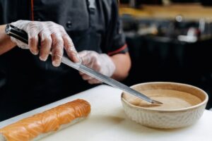 Ein Koch taucht sein Sushi Messer im Wasser, um eine Sushi Rolle zu schneiden.