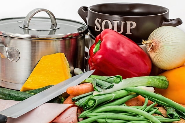 Auf dem Bild sind ein Topf, eine Suppenschüssel, ein Messer und verschiedene Lebensmittel zu sehen.