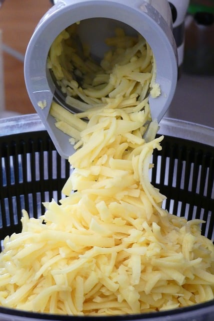 Nahaufnahme einer elektrischen Reibe, mit der Käse gerieben wird.